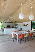 Dining table with colourful classic chairs below spherical lamps in high-ceilinged open-plan interior
