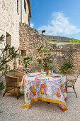 Set table with colourful tablecloth on gravelled area in front of natural stone house