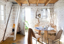 Round table with chairs, ladder to attic and garden access in room with whitewashed brick wall