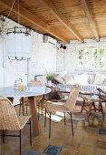 Breakfast table with chairs, in the background sofa with cushions in the room with whitewashed brick wall