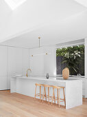 Elegante Kücheninsel mit Marmorplatte und Barhockern in weißer Küche mit Fenster