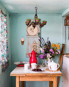 A beaded chandelier above a small table with a summer picnic and wild flowers in a beachhut with a vintage curtain