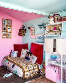 Cushions on a daybed next to a crockery cupboard in a beach hut with pink and blue walls