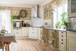 Cream-coloured kitchen units, splashback with subway tiles, floral wallpaper and plate rack in open-plan kitchen