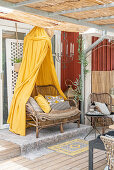 Rattansofa mit gelbem Betthimmel auf der Terrasse