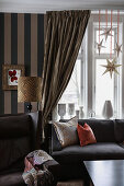 Armchair, sofa and window decorated for Christmas in room with curtains and striped wallpaper