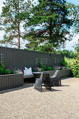 Moderne Gartenstühle vor Bank zwischen zwei Hochbeeten an Sichtschutzwand in Grau