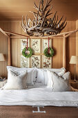 Doppelbett mit Holzgestell, darüber Geweih-Kronleuchter im Schlafzimmer mit Holzverkleidung