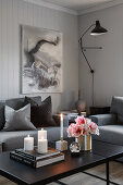 Candles and flowers on black coffee table and grey upholstered furniture in living room