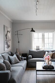 Candles and flowers on black coffee table and grey upholstered furniture with scatter cushions in living room