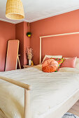 Simple wooden bed in bedroom with terracotta-coloured walls