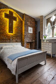 Guest bedroom with double bed below illuminated cross on brick wall