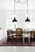 Wooden dining table with various chairs below pendant lights in white room