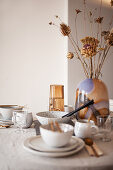 Gedeckter Tisch mit Leinendecke, Keramikgeschirr, Glasvase und Trockengräsern