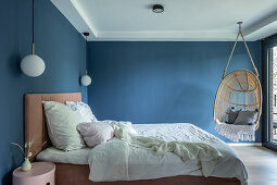 Double bed and hanging chair in bedroom with blue walls
