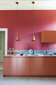 Kitchen base units below pendant lights in front of red wall
