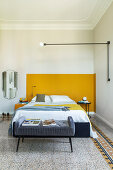 Upholstered bedroom bench and double bed in front of yellow wall in bedroom