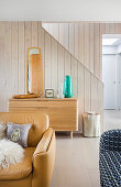 Buff leather armchair and sideboard in front of staircase wall with wooden panelling