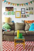 Sofa with scatter cushions below pictures and bunting on the wall and small table on polka-dot rug