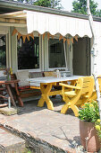 Yellow-painted wooden table with chairs and bench on terrace