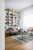View into living room with floor-to-ceiling bookshelf, sofa and coffee table on a striped rug