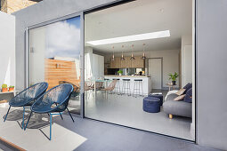 Outdoor chairs in front of sliding glass door on terrace with view into open-plan interior