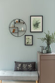 Bench and cabinet below round shelf module and botanical prints on green wall