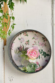 Small vase holding rose 'Eden Rose' in old springform tin backed with floral wallpaper
