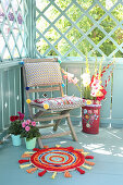 DIY patchwork rug made of colourful fabric scraps, dahlias, gladioli and wooden chair with cushions on balcony