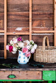 Üppiger Rosenstrauß in Krugvase und Korb auf Holztisch