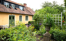 Urne auf Steinsockel und Rankgitter im Frühlingsgarten vor dem Haus