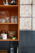 A kitchen shelf with crockery, photo wallpaper and black tiles