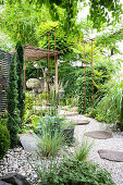 Kiesweg mit Trittplatten und bewachsene Pergola im Garten