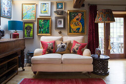 Cushions with dog motifs on cosy two-seater in front of gallery of pictures in rustic room