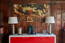 Modern sideboard with table lamps above it Paintings in the room with dark coffered panelling