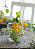 Glasvase umwickelt mit Clematis-Fruchtständen, gefüllt mit Ringelblumem (Calendula officinalis)