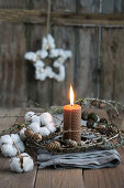 Rolled beeswax candle with a wreath of larch cones and cotton on a linen cloth
