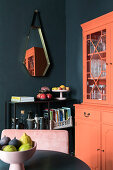 Blick über runden Tisch auf Regal und orangefarbener Anrichte im Zimmer mit schwarzen Wänden