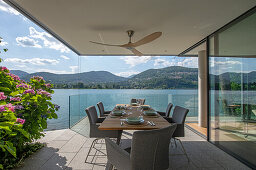 Dining table on covered terrace with glass balustrade panels and lake view