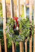 Weihnachtlicher Kranz mit roter Schleife hängt am Staketenzaun aus Kastanie
