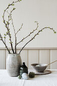 Ceramic vase of branches on Easter table set with naturally coloured Easter eggs