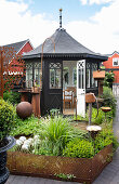 Black painted gazebo and small flower bed with rusty fence