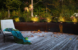 Wooden terrace with lounger, in the background illuminated raised beds made of rusty corten steel