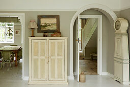Cream-colored cupboard and grandfather clock in a room with a view into dining area and hallway