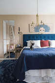 Blaues Bett mit blauer Tagesdecke und Katze im hellen Schlafzimmer in Beigetönen