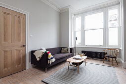 Anthrazitfarbenes Sofa und Couchtisch im Zimmer mit hellgrauen Wänden und Stuckarbeit