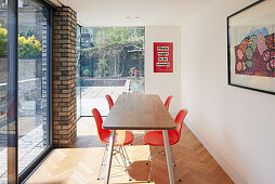 Red shell chairs in a narrow dining room with floor to ceiling windows