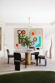 Round table with brass base and marble top, designer chairs, and modern art in the dining area