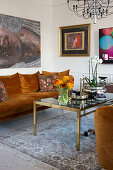 Braun-orangefarbenes Plüschsofa mit Kissen, darüber Kunstwerke und Couchtisch mit Glasplatte in hellem Wohnzimmer