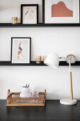 Schwarze Regalbretter mit Bildern an weißen Wand über dem Schreibtisch